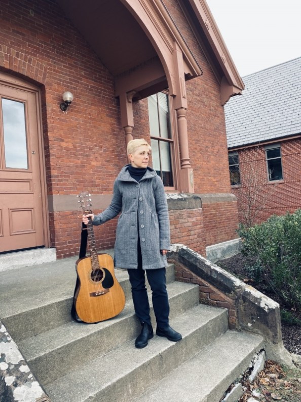 Erin Ash Sullivan holding a guitar on the steps of building