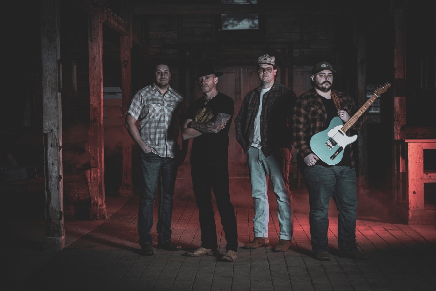 Midnight South band photo: four men stand inside a barn, one of them with a guitar strapped over his shoulder